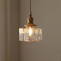 Vintage-style pendant light with clear glass shade and brass fixture on a neutral background